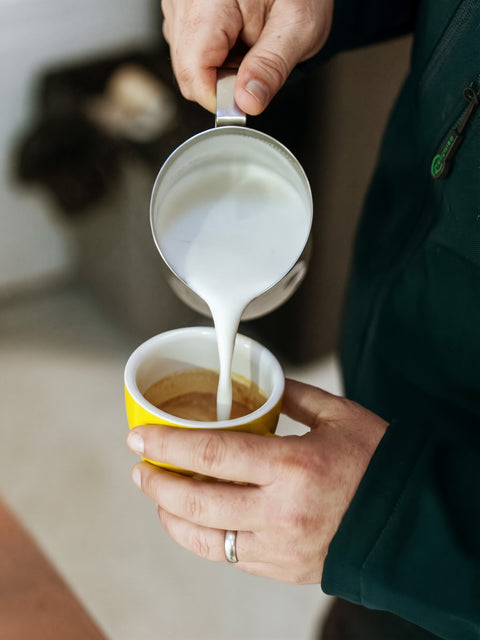 Pouring steamed milk into a coffee in a yellow cup